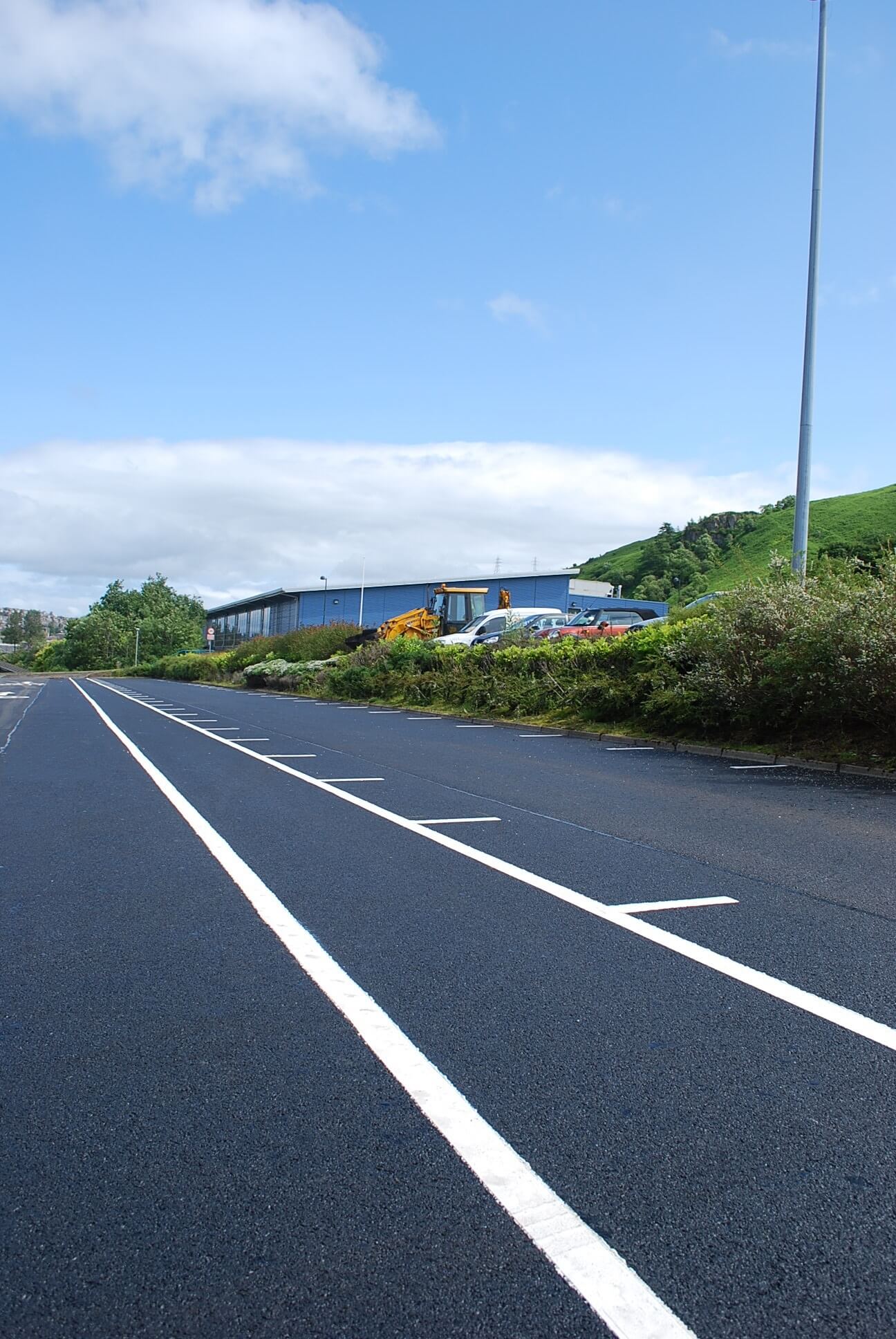 newly tarmacked road lined next to cars with a blue sky